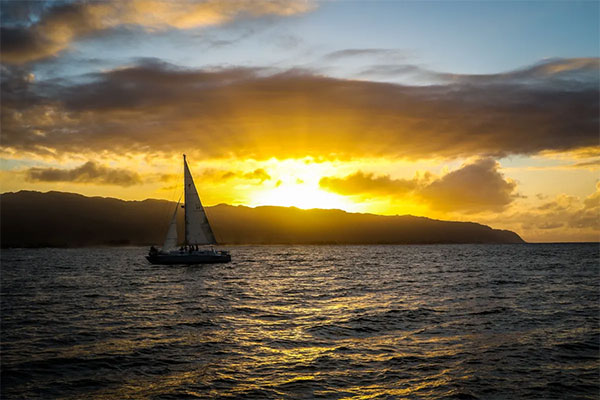 Sailboat on a sunset cruise off the coast of Oahu, Hawaii, with golden light over the ocean horizon.